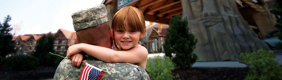 A girl smiles at the camera as her military father carries her toward a Great Wolf Lodge entrance.